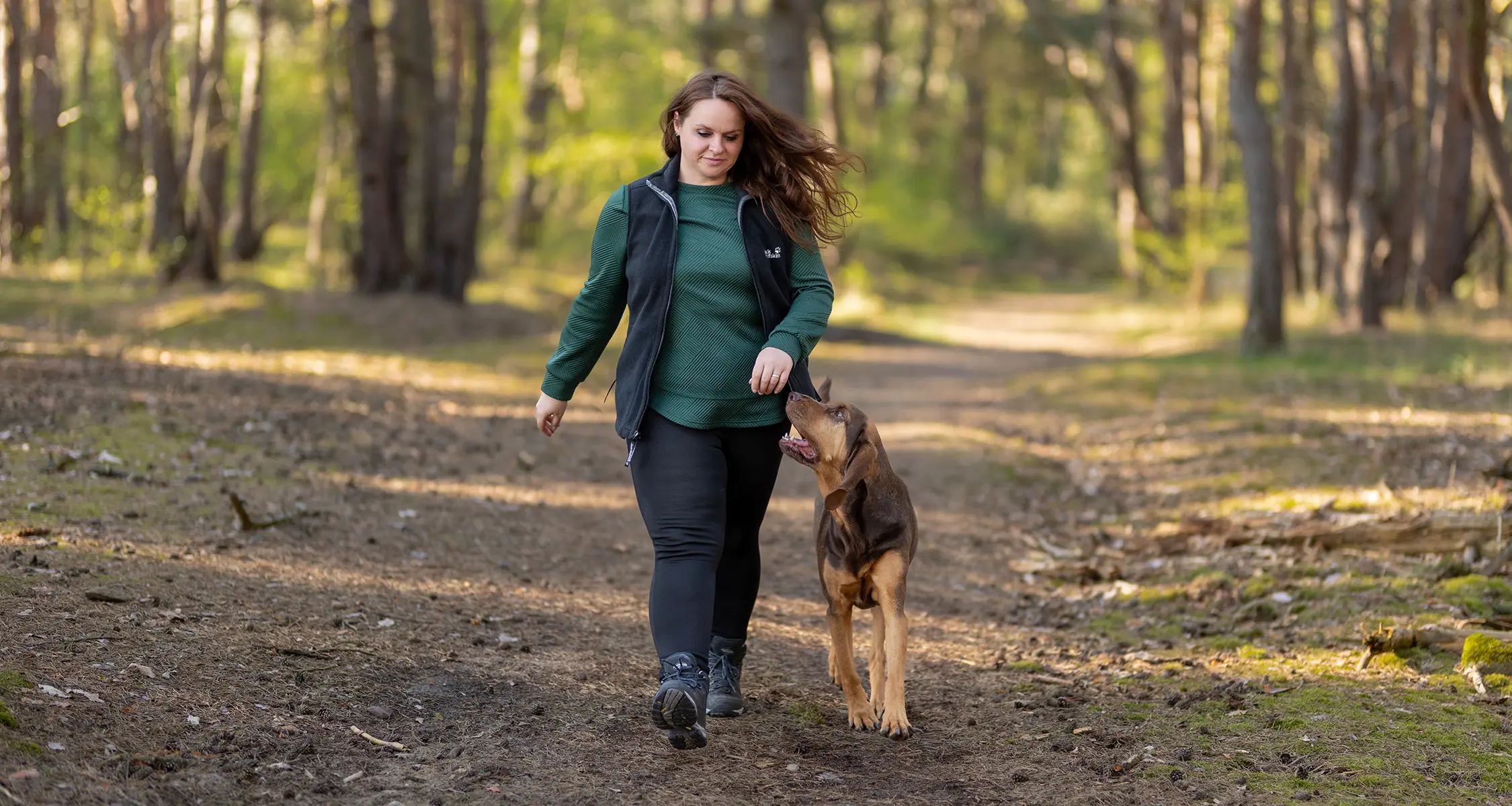 Hundetrainerin Caroline Rehmer geht mit Hund bei einem geführten Spaziergang im Wald