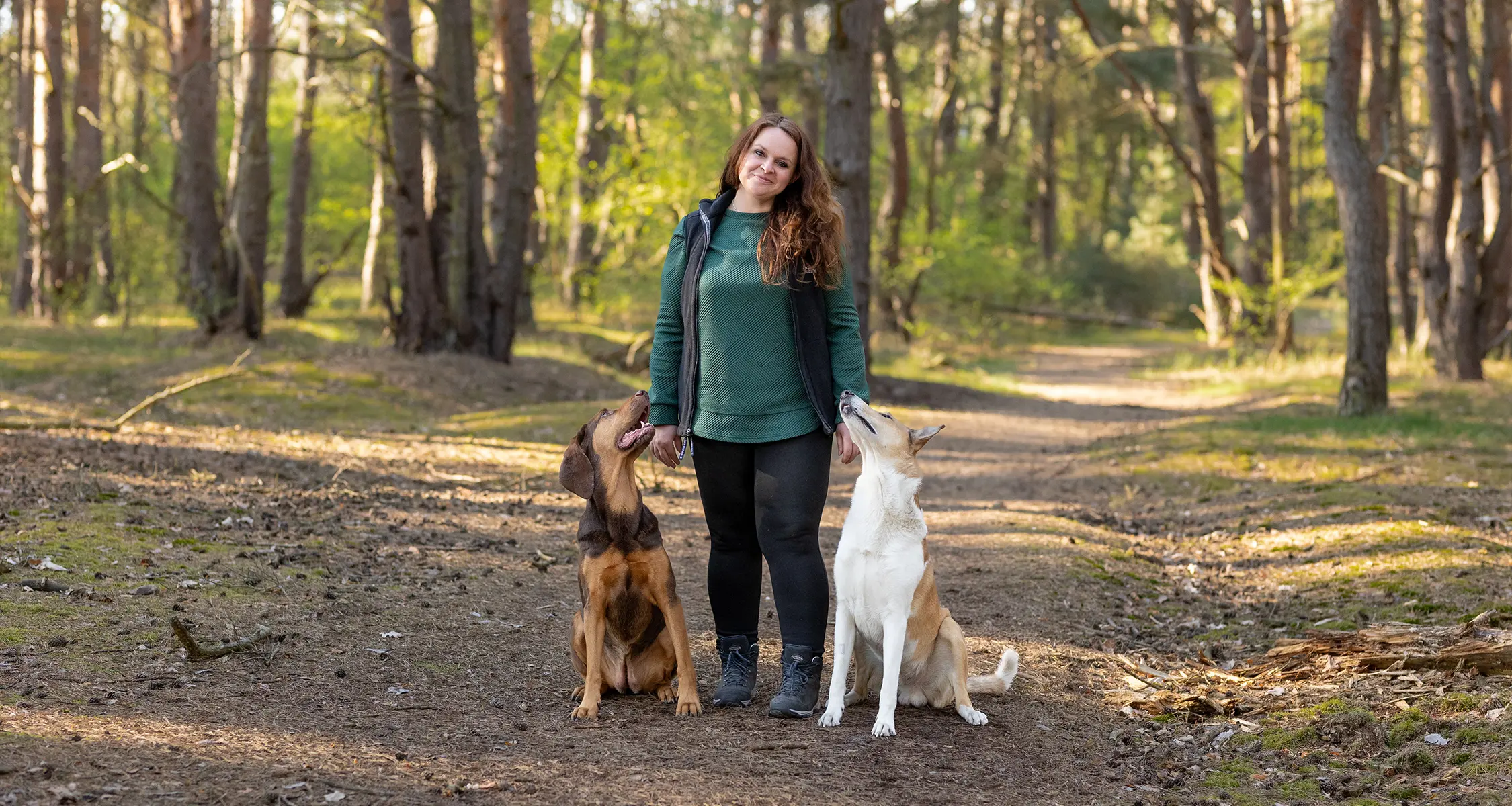 Caroline Rehmer steht im Wald mit ihren zwei Hunden Hazel und Kurama